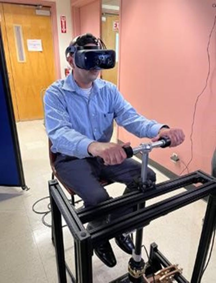 A participant wearing a VR headset rides a physical scooter handlebar mounted on a steering base
